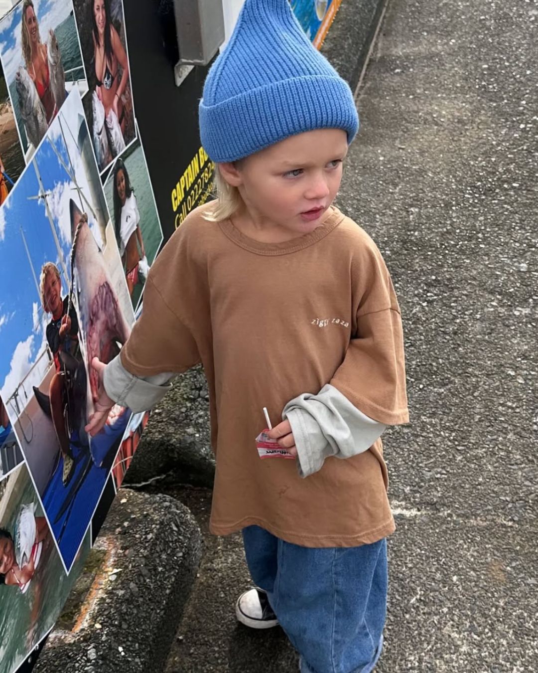 Child wearing a blue beanie and brown shirt standing on a street.