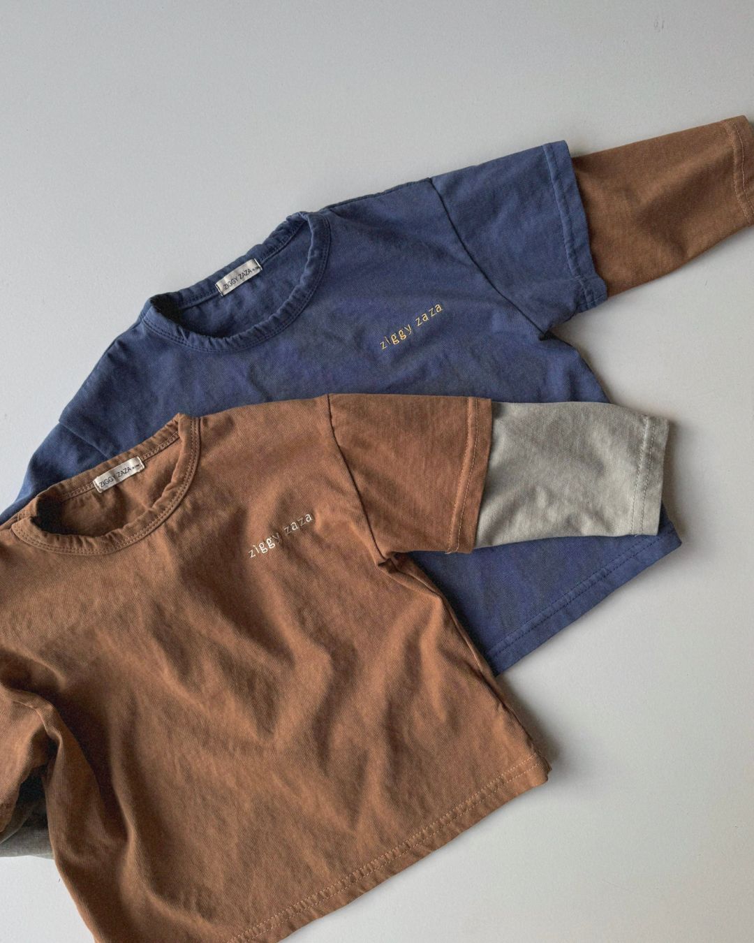 two tee shirts in brown and blue on a light gray background.